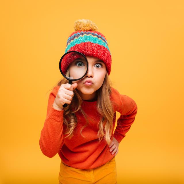 joyeuse-jeune-fille-pull-chapeau-regardant-camera-loupe-orange.jpg